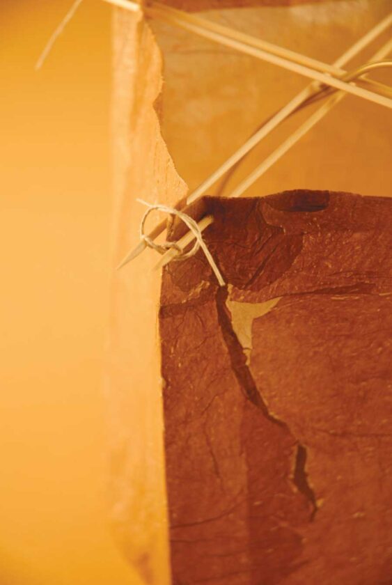 At each corner, squeeze skewers together and fold corner creases outward, forcing lampshade into a crisp, rectangular shape. Cut a 6- to 12-inch piece of twine or thin wire and tie. Adjust so lampshade hangs straight and square.